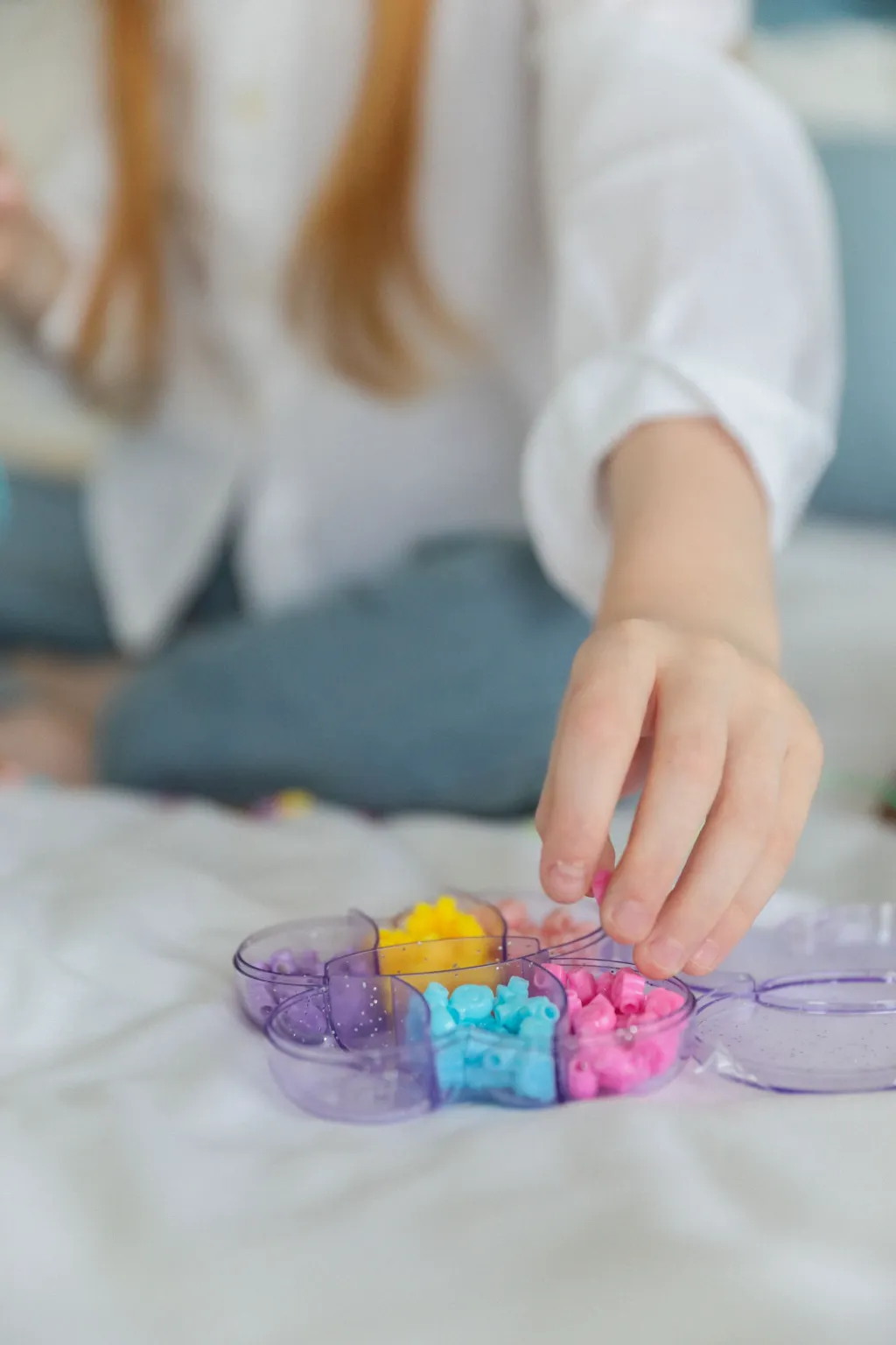 Un enfant assis en tailleur prend des perles colorées dans une boîte